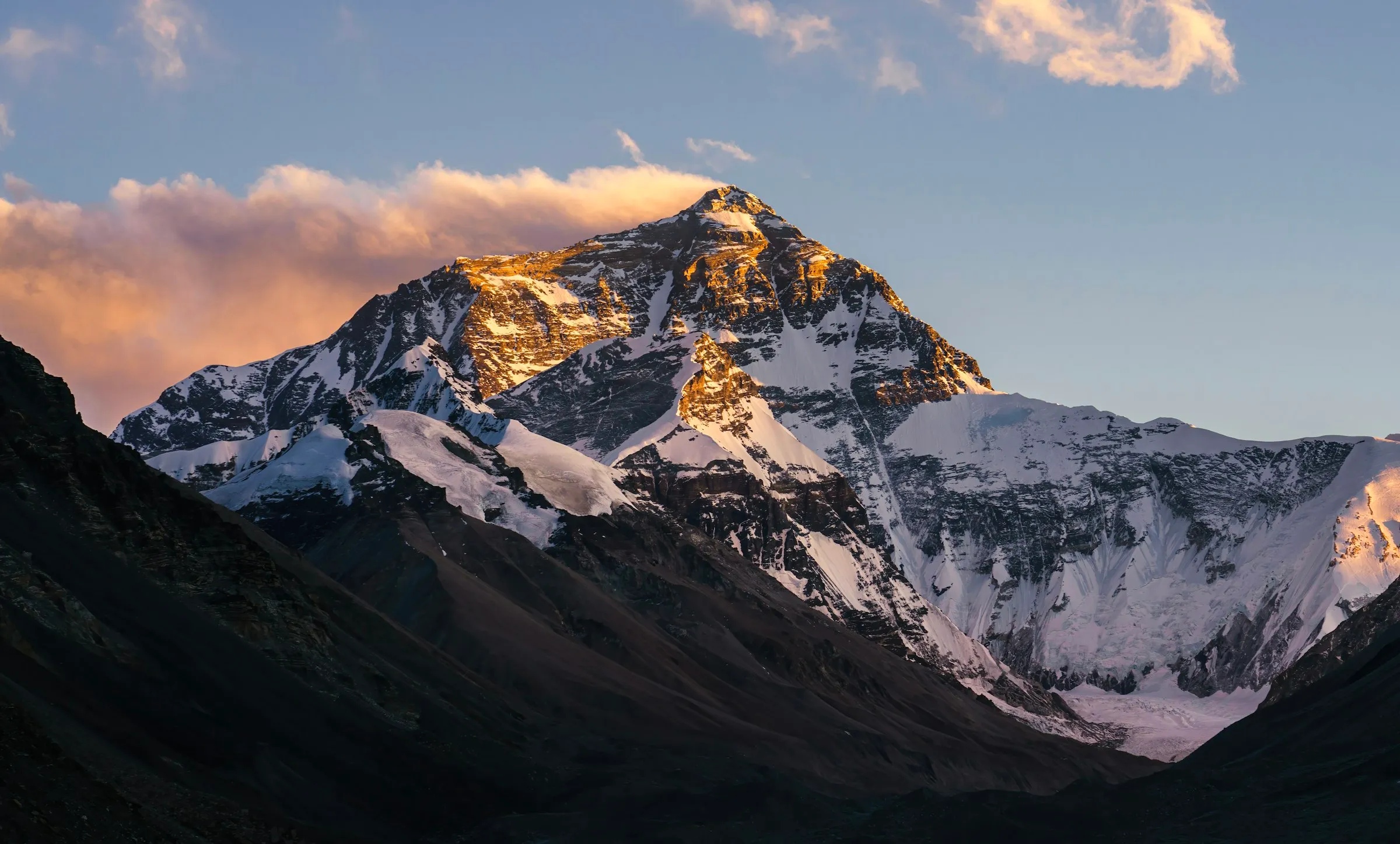 Mount Everest's summit lit gold at sunset, cloud plume streaming off the peak
